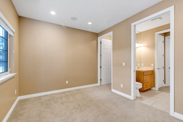 unfurnished bedroom with light colored carpet, ensuite bathroom, and sink