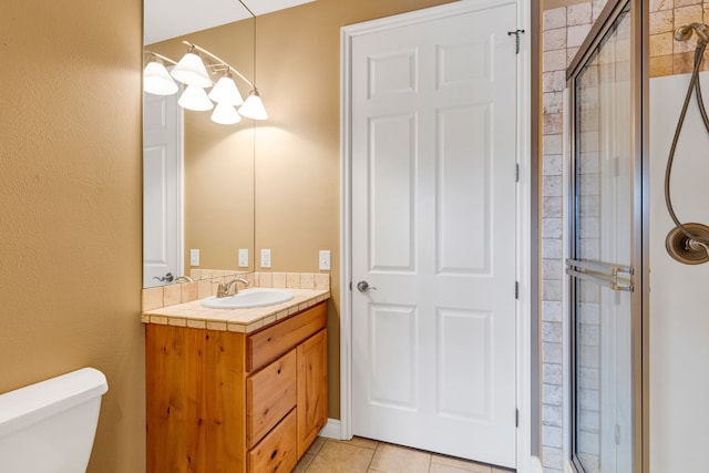 bathroom with a shower with door, vanity, tile patterned floors, and toilet