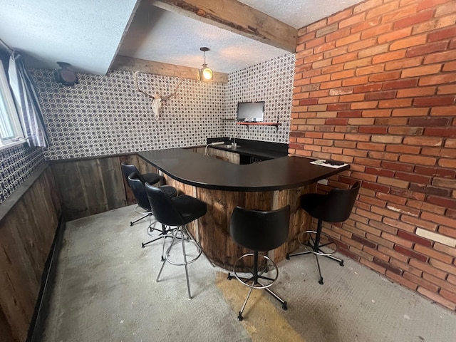 bar featuring beamed ceiling, a textured ceiling, and brick wall