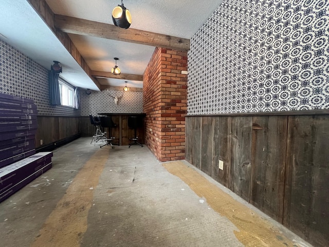 additional living space featuring beamed ceiling, indoor bar, a textured ceiling, and wood walls