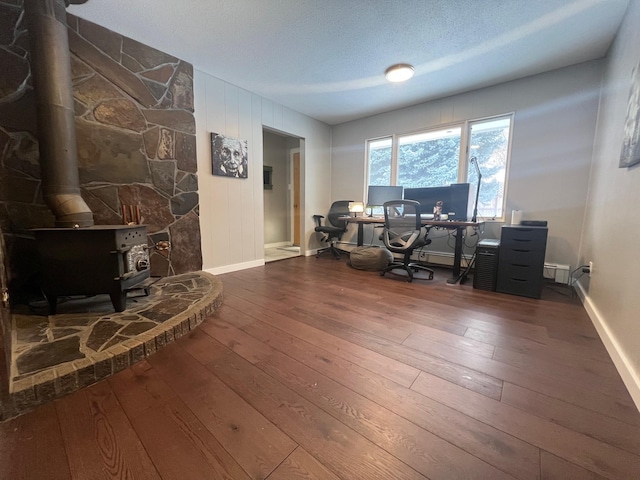 office space with wood-type flooring, a textured ceiling, and a wood stove