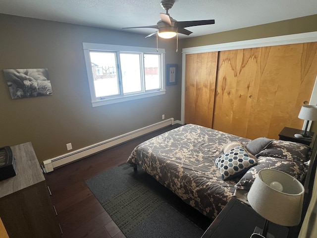 bedroom with ceiling fan, a baseboard heating unit, a textured ceiling, dark hardwood / wood-style flooring, and a closet