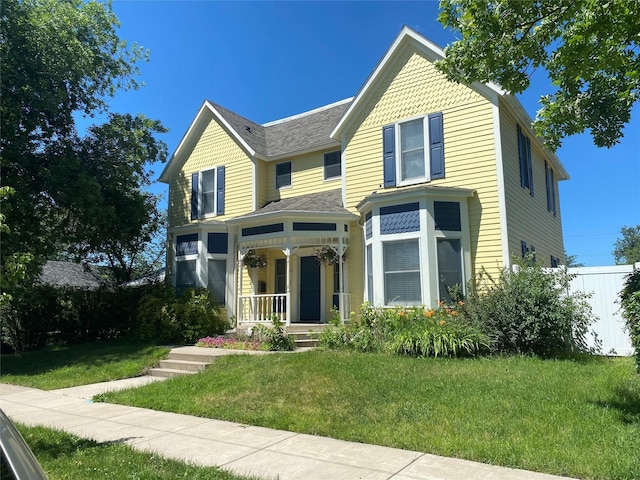 victorian house with a front yard, covered porch, and fence