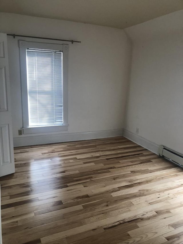 spare room featuring a baseboard radiator, wood finished floors, and baseboards