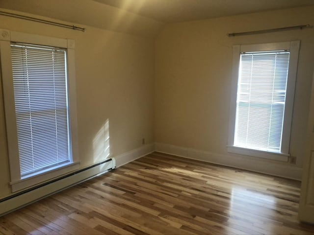 unfurnished room with a baseboard heating unit, vaulted ceiling, baseboards, and wood finished floors