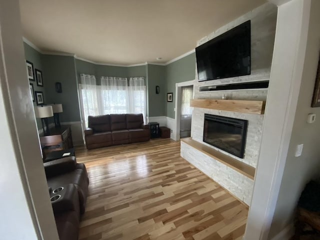 living area featuring crown molding, baseboards, wood finished floors, and a stone fireplace