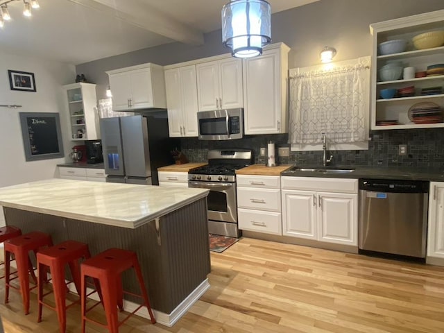 kitchen featuring a breakfast bar area, a sink, appliances with stainless steel finishes, decorative backsplash, and open shelves