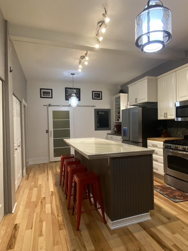 kitchen featuring stainless steel appliances, white cabinetry, light wood-style floors, backsplash, and a center island