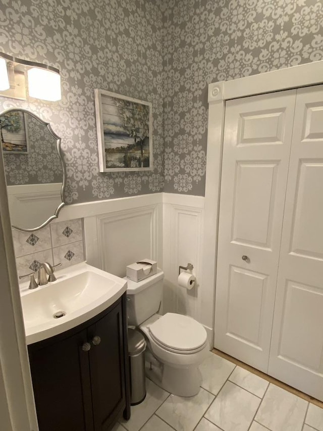 bathroom featuring wainscoting, vanity, toilet, and wallpapered walls