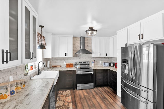 kitchen with appliances with stainless steel finishes, sink, hanging light fixtures, light stone countertops, and wall chimney range hood