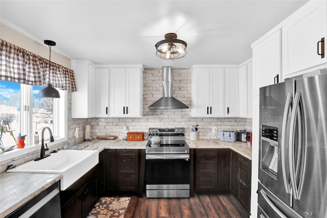 kitchen with decorative light fixtures, white cabinetry, sink, stainless steel appliances, and wall chimney exhaust hood