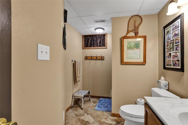 bathroom featuring vanity, toilet, and a drop ceiling