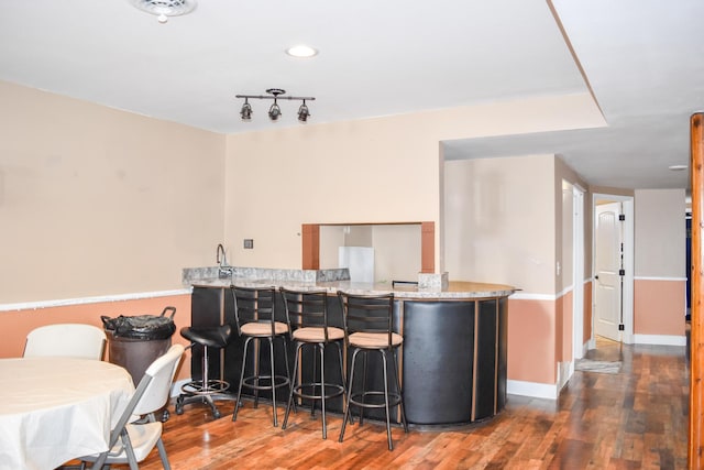 kitchen with light stone counters, hardwood / wood-style flooring, kitchen peninsula, and a kitchen bar