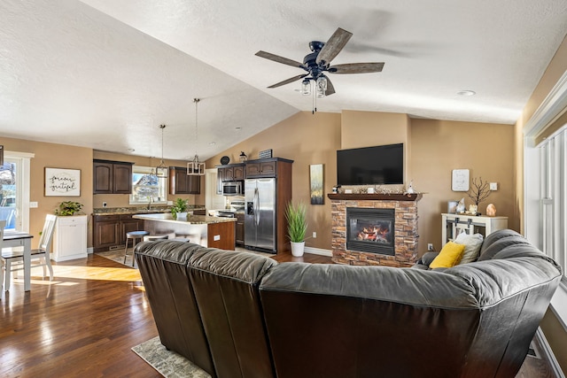 living room featuring vaulted ceiling, a stone fireplace, sink, dark hardwood / wood-style flooring, and a textured ceiling