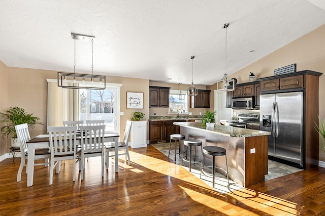 kitchen with a kitchen island, appliances with stainless steel finishes, dark brown cabinetry, and decorative light fixtures