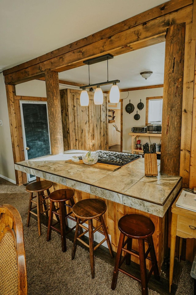 interior space featuring hanging light fixtures, a kitchen breakfast bar, dark colored carpet, ornamental molding, and beamed ceiling