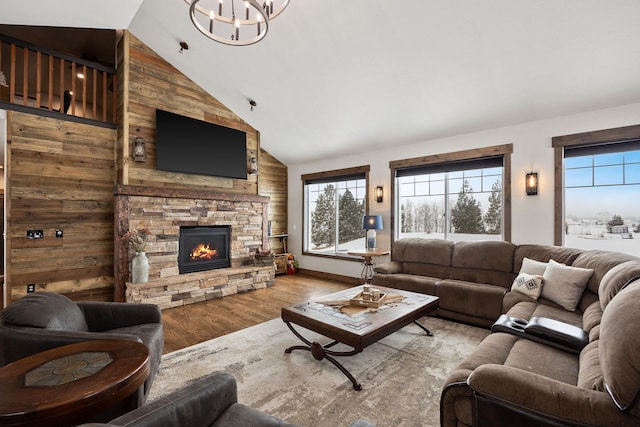 living room with a notable chandelier, a stone fireplace, high vaulted ceiling, and light wood-type flooring