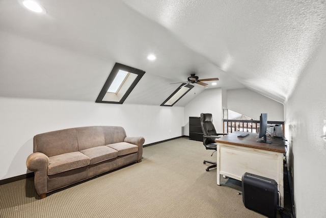 carpeted office space featuring ceiling fan, lofted ceiling with skylight, and a textured ceiling