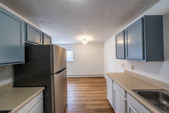 kitchen with a baseboard heating unit, sink, stainless steel fridge, and light hardwood / wood-style floors