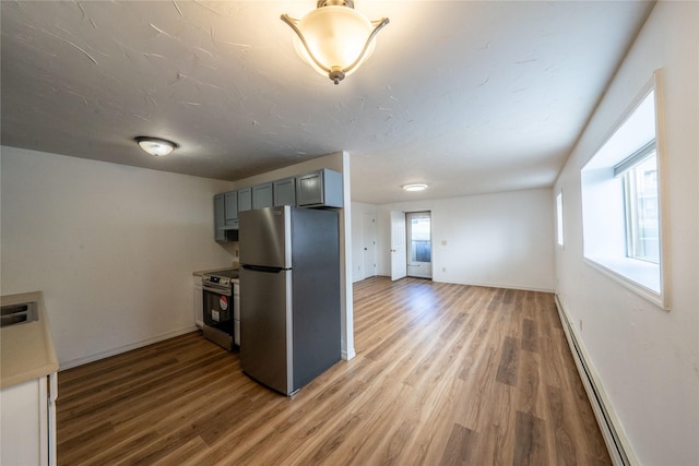 kitchen with gray cabinetry, hardwood / wood-style flooring, a baseboard radiator, and appliances with stainless steel finishes