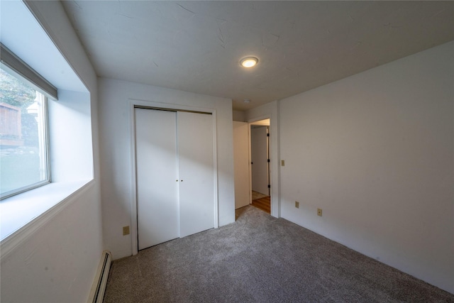 unfurnished bedroom featuring a baseboard heating unit, carpet flooring, and a closet