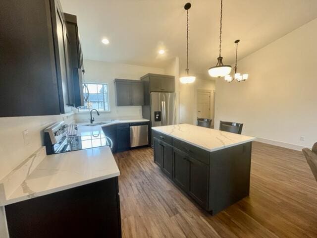 kitchen with pendant lighting, sink, stainless steel appliances, light stone counters, and a kitchen island