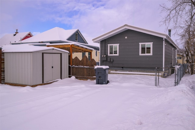 snow covered rear of property featuring a shed, an outdoor structure, fence, and a gate