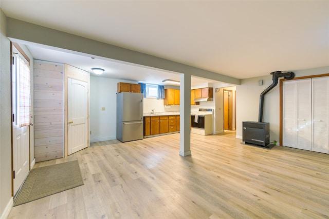 unfurnished living room with a wood stove, a sink, light wood-style flooring, and baseboards