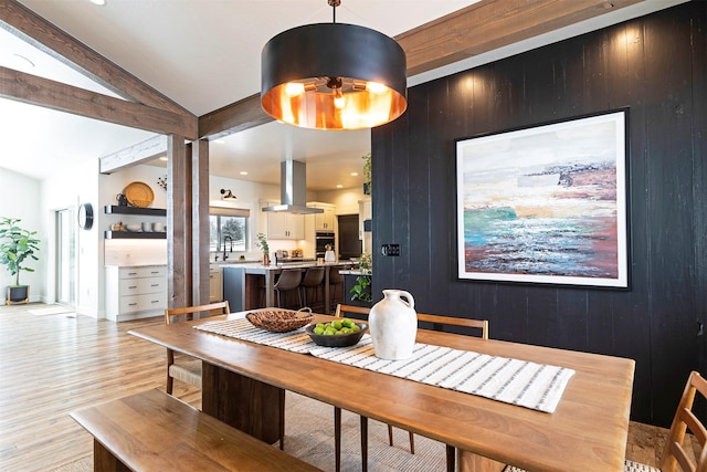 dining space featuring vaulted ceiling with beams, wooden walls, and light wood-type flooring