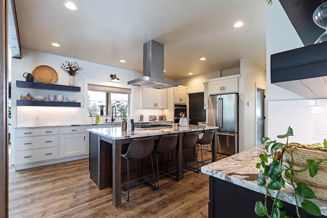 kitchen with white cabinetry, stainless steel appliances, a kitchen breakfast bar, and island exhaust hood