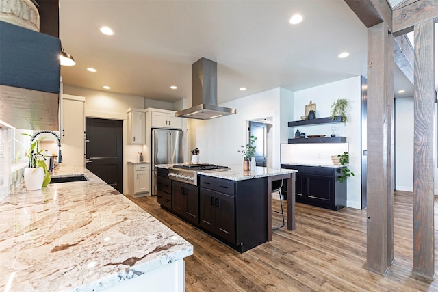 kitchen with sink, light stone counters, island exhaust hood, stainless steel appliances, and white cabinets