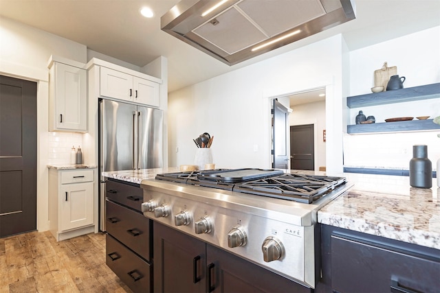 kitchen featuring wall chimney range hood, appliances with stainless steel finishes, backsplash, light hardwood / wood-style floors, and white cabinets