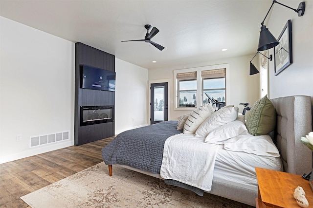 bedroom featuring hardwood / wood-style flooring, ceiling fan, a fireplace, and access to exterior