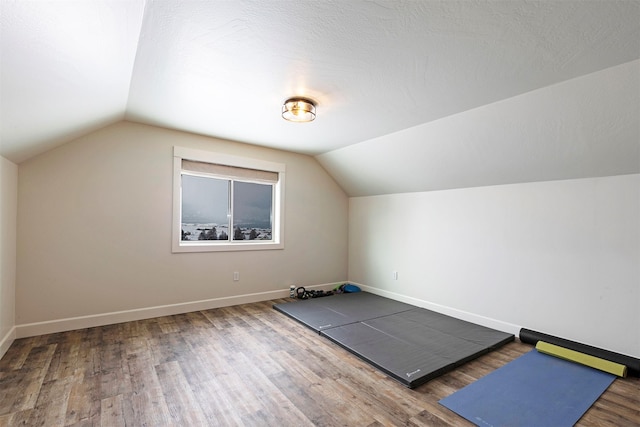 exercise room with hardwood / wood-style floors, vaulted ceiling, and a textured ceiling