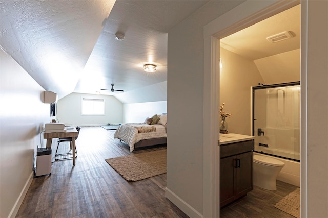 bedroom featuring dark wood-type flooring, lofted ceiling, connected bathroom, and a textured ceiling