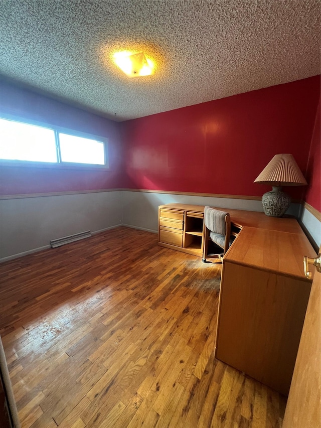 unfurnished office with a textured ceiling, wood finished floors, visible vents, and baseboards