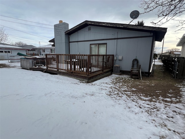 snow covered rear of property with a chimney, fence, central AC, and a wooden deck