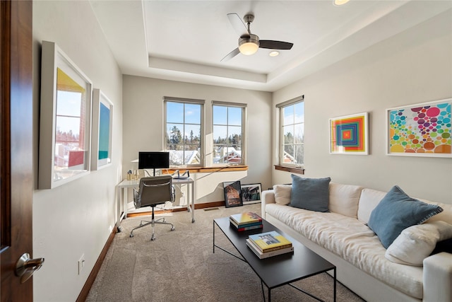 home office featuring ceiling fan, carpet flooring, and a tray ceiling