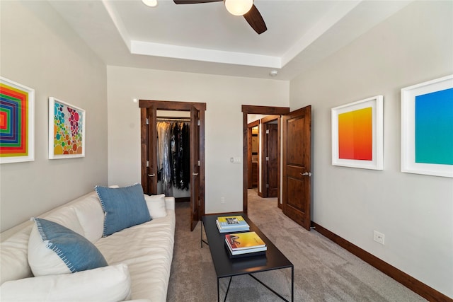 carpeted living room with ceiling fan and a tray ceiling