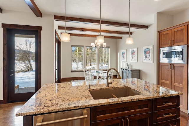 kitchen featuring sink, appliances with stainless steel finishes, a kitchen island with sink, hanging light fixtures, and light stone counters