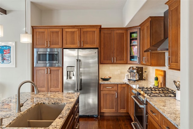 kitchen with sink, hanging light fixtures, high end appliances, light stone countertops, and wall chimney exhaust hood