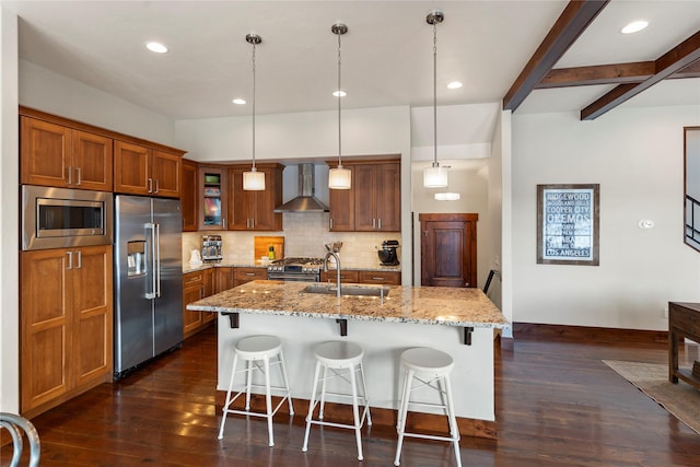 kitchen with sink, a center island with sink, pendant lighting, stainless steel appliances, and wall chimney range hood