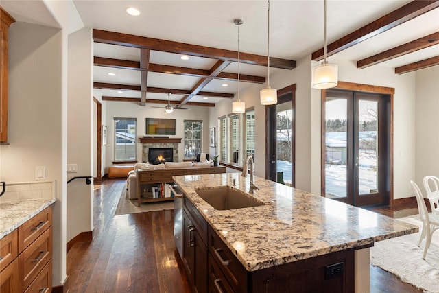 kitchen featuring light stone counters, sink, hanging light fixtures, and an island with sink