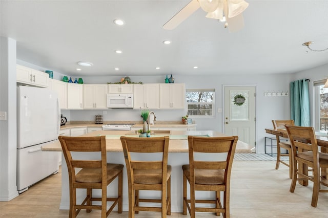 kitchen with white cabinetry, a kitchen breakfast bar, a kitchen island with sink, white appliances, and light hardwood / wood-style flooring