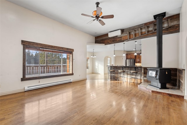 living room with baseboard heating, ceiling fan, light hardwood / wood-style floors, a wall unit AC, and a wood stove