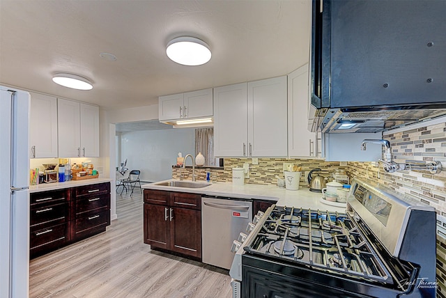 kitchen with stainless steel appliances, a sink, white cabinets, light countertops, and light wood finished floors