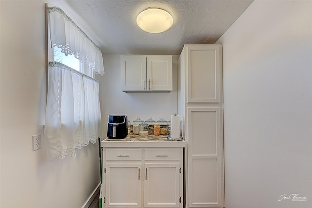 kitchen with a textured ceiling, light countertops, and white cabinets