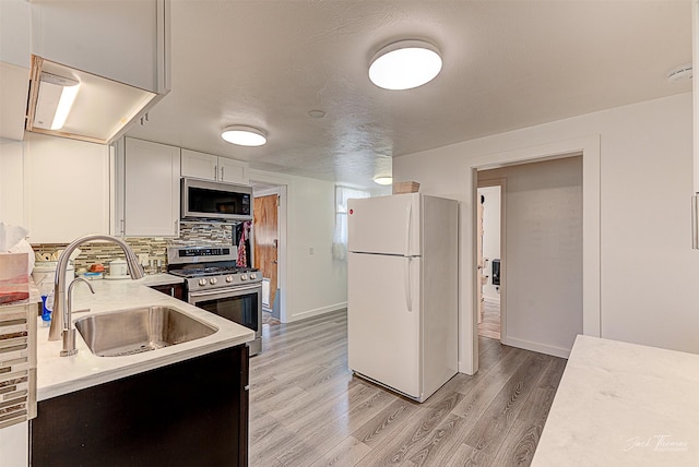 kitchen featuring a sink, light countertops, appliances with stainless steel finishes, backsplash, and light wood finished floors