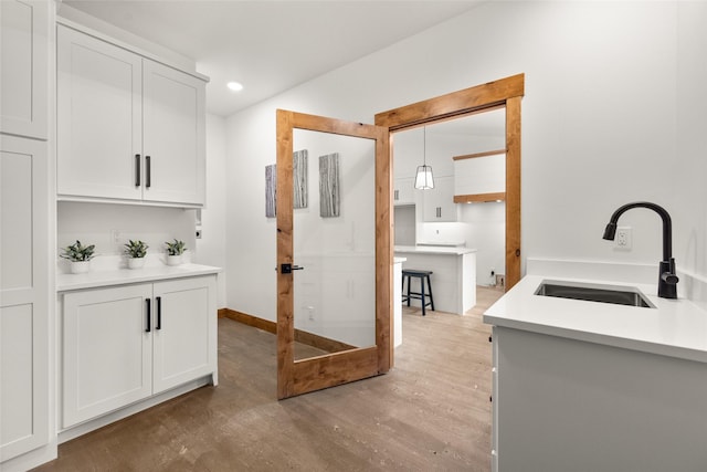 interior space with hardwood / wood-style flooring, white cabinetry, sink, and pendant lighting