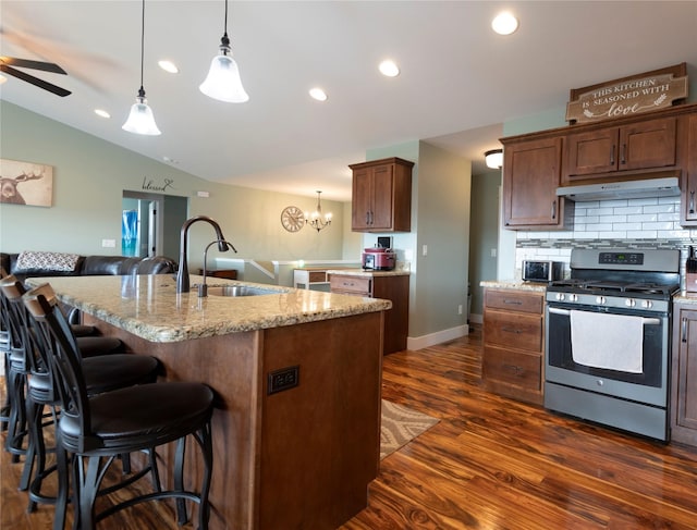 kitchen with lofted ceiling, sink, a kitchen island with sink, stainless steel gas range oven, and decorative light fixtures